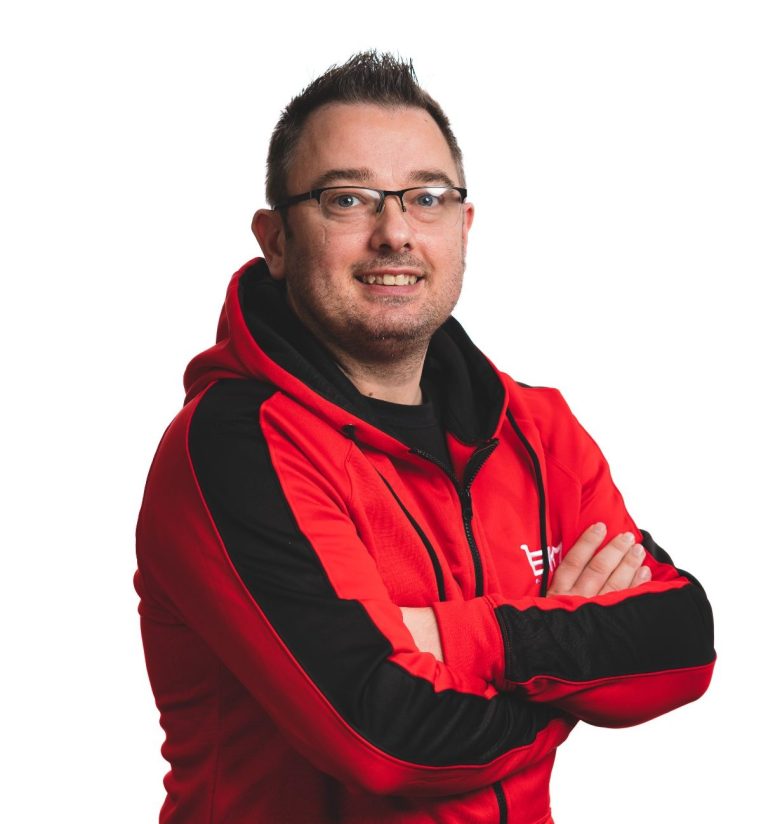 Smiling man in a red jacket with a black stripe, arms crossed, wearing glasses.