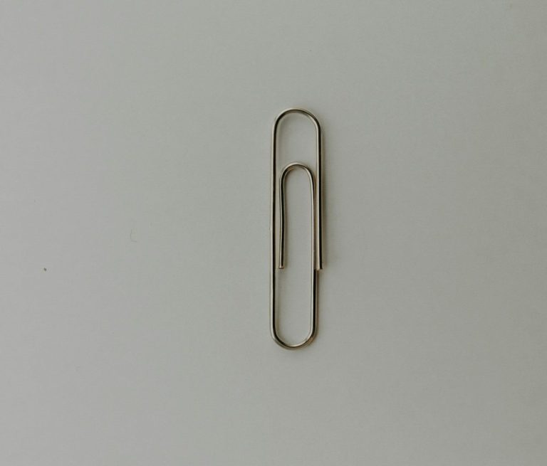 A metallic paper clip lying flat on a neutral background.